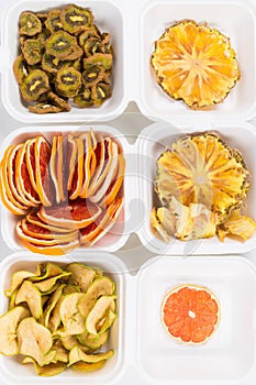 The plastic white containers contain sliced dried fruits, apple, kiwi, pineapple and grapefruit