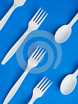 Plastic white disposable fork and spoon on a trendy blue color background. Concept plastic dishes, fast food, plastic pollution.