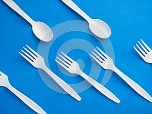 Plastic white disposable fork and spoon on a trendy blue color background. Concept plastic dishes, fast food, plastic pollution.