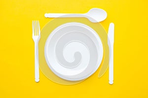 Plastic white fork, knife, spoon and plate on yellow background. Cooking utensil. Top view. Minimalist Style. Copy, empty space