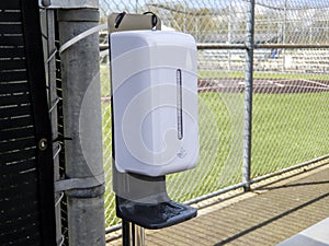 A plastic white hand sanitizer dispenser outside of a baseball field