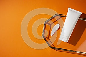 Plastic white tube for lotion and the appearance of the texture of the cream in glass tray on orange background.