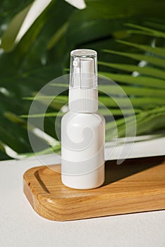 Plastic white tube for lotion with pomp on wooden plate against the background of palm leaves.