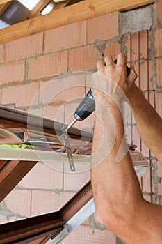 Plastic window installation. Worker attaches anchor plate with screwdriver.