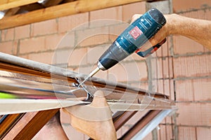 Plastic window installation. Worker attaches anchor plate with screwdriver. photo