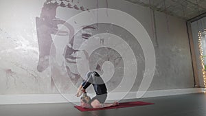 Plastic woman with tattoos is engaged in aerobics against the background of a wall with the image of a Buddha