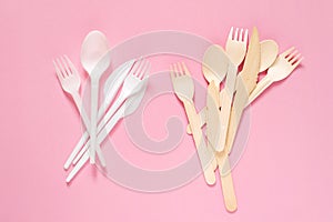Plastic and wooden forks, spoons and knives on a pink surface close-up, top view. No plastic, eco tableware, biodegradable tablewa