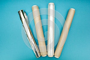 Plastic wrap, aluminum foil and roll of parchment paper on blue background