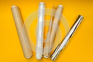 Plastic wrap, aluminum foil and roll of parchment paper on yellow background