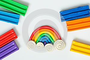 Plasticine rainbow with clouds and pieces of clay on white background