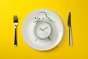 Plate with alarm clock, fork and knife on background, top view