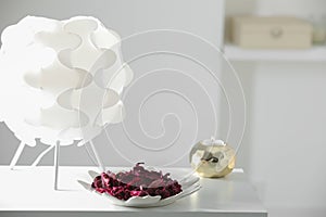 Plate with aromatic potpourri, lamp and burning candle on white table in room
