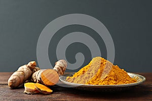 Plate with aromatic turmeric powder and cut roots on wooden table. Space for text