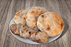 Three Pitta Bread Loaves And Baguette Bread Slices On Porcelain Plate Set On Grayish Brown Wood Background