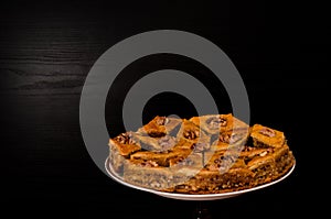 A plate of baklava with honey on a black background, traditional Turkish sweets. Rombus