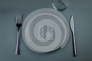 plate with blister packs of medicine pills, fork and knife - concept for food problems, drug abuse, chemical feeding