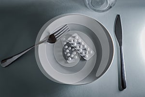 plate with blister packs of medicine pills, fork and knife - concept for food problems, drug abuse, chemical feeding