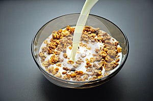 A plate bowl of cereal oatmeal and milk. Milk is pouring in a plate on a dark background. Healthy breakfast. Proper nutrition.