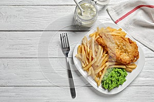 Plate with British traditional fish and potato chips on wooden background, top view.