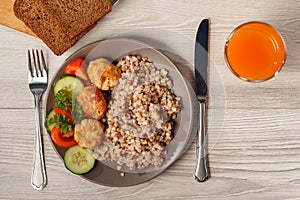 Plate with buckwheat, fried meat cutlets, pieces of fresh cucumbers and tomatoes decorated with branch of fresh parsley with