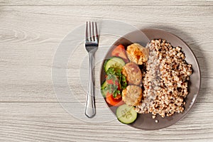 Plate with buckwheat, fried meat cutlets, pieces of fresh cucumbers and tomatoes decorated with branch of fresh parsley with fork