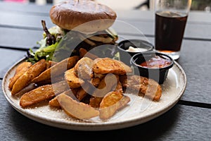 Plate with burger and french fries, ketchup and mayonnaise and cola on the table.