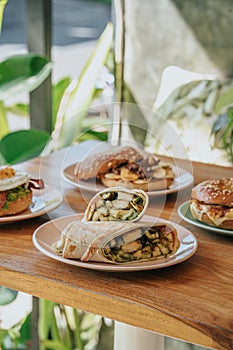 A plate of burrito and bagel burger with chicken parmesan, fried, sauce, and cheese on a wooden table