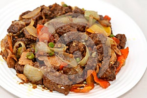 A plate of Chinese food cuisine of grilled beef red meat pieces with oil, mushroom, vegetables, peas, carrots, colorful peppers,