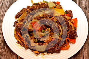 A plate of Chinese food cuisine of grilled beef red meat pieces with oil, mushroom, vegetables, peas, carrots, colorful peppers,