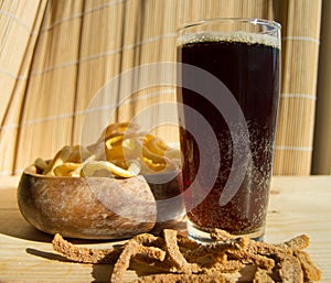 Plate of chips, glass of dark beer with foam, bubbles and crackers on wooden background