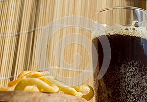 Plate of chips, a glass of dark beer with foam, bubbles on wooden background