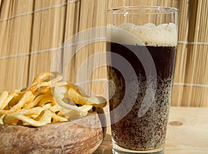 Plate of chips, a glass of dark beer with foam, bubbles on wooden background
