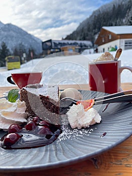 a plate of chocolate cake cherry sauce and ice cream with a bokeh background of two cups, snow and a ski lift