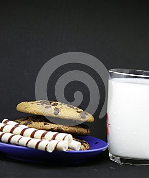 A plate of chocolate chip cookies on a blue plate with a glass of milk on a black background close-up