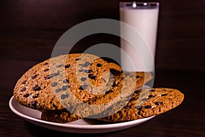 Plate with chocolate chip cookies and a glass of milk on a dark wooden table