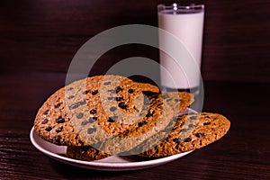 Plate with chocolate chip cookies and a glass of milk on a dark wooden table