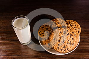 Plate with chocolate chip cookies and a glass of milk on a dark wooden table