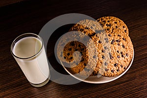 Plate with chocolate chip cookies and a glass of milk on a dark wooden table
