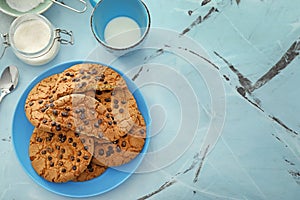 Plate with chocolate chip cookies and milk on color background