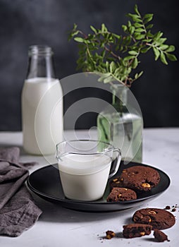 Plate with Chocolate cookies with nuts and glass of milk on dark background. Nordic style