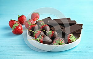 Plate with chocolate covered strawberries and bars on wooden table
