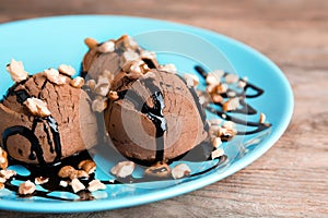 Plate of chocolate ice cream with nuts on wooden table, closeup