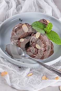 Plate of chocolate ice cream scoops with almond and mint leaf on white background