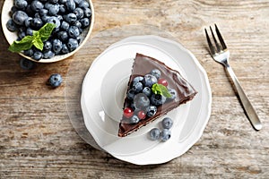 Plate with chocolate sponge berry cake and bowl of berries on wooden background