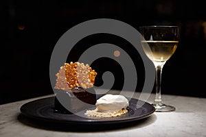 Plate of chocolate and white dessert next to a glass of white whine on a table