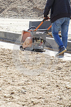 Plate compactor for for soil compaction pavement or sidewalk in the city. Worker is compacting soil by vibratory plate
