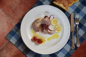 A plate of cooked small polyp and lemons garnished in olive oil on a ceramic table with old cutlery photographed from above