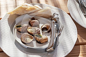 A plate with cooked snails and cutlery for eating snails.