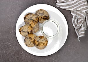 Plate with cookies, chocolate pieces, a glass of milk on a brown background, top view.