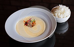 Plate of corn soup with a bowl of rice on a reflective surface